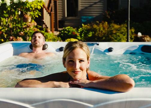 A couple talking in a hot tub with fireplace and lake in the background.